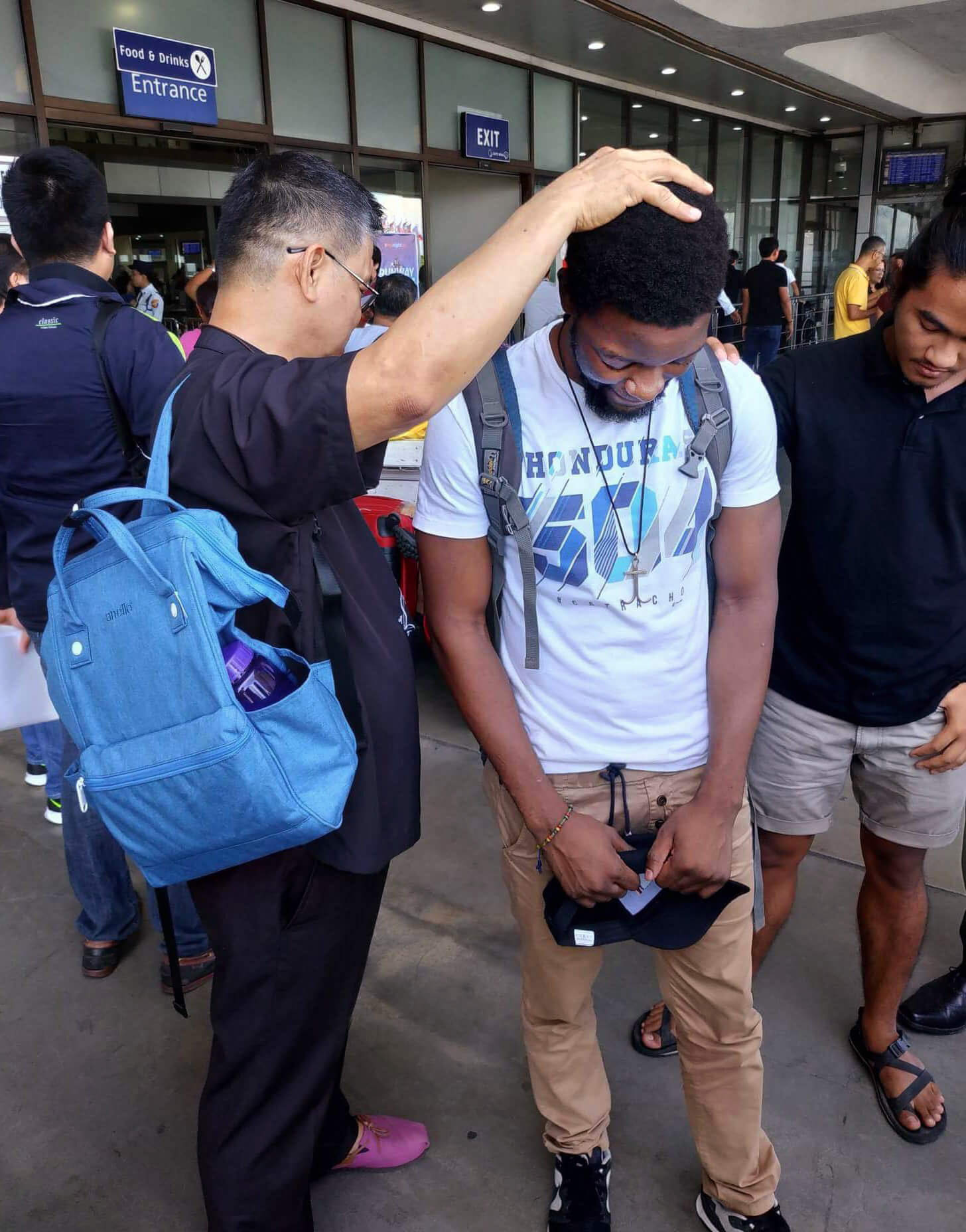 Bishop Ciriaco Q. Francisco (left) of the Manila Episcopal Area prays with Tawanda Chandiwana outside the Ninoy Aquino International Airport after the United Methodist missionary was released from a detention center and allowed to leave the Philippines. Photo courtesy of Thomas Kemper, GBGM.