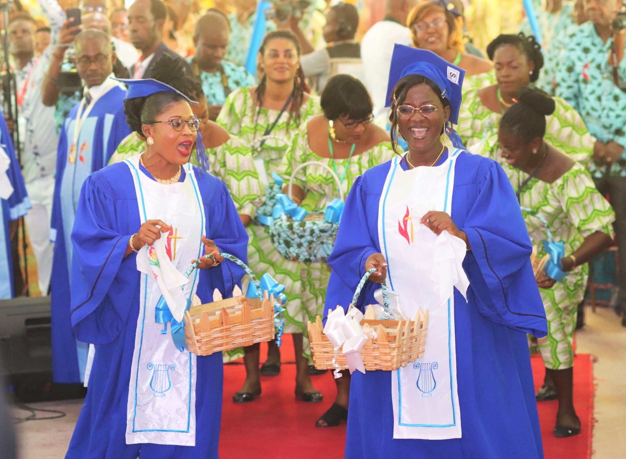 Les choristes Marceline Allyko (à gauche) et Marina Gangan apportent devant l’autel les dons de reconnaissance des fidèles pour le 25ème anniversaire du temple de la Cité de grâce d’Anoumabo. Troisième temple construit en matériaux durables depuis l’avènement du Méthodisme dans ce village, il a été dédicacé le 27 février 1994. Photo de Isaac Broune, UM News.