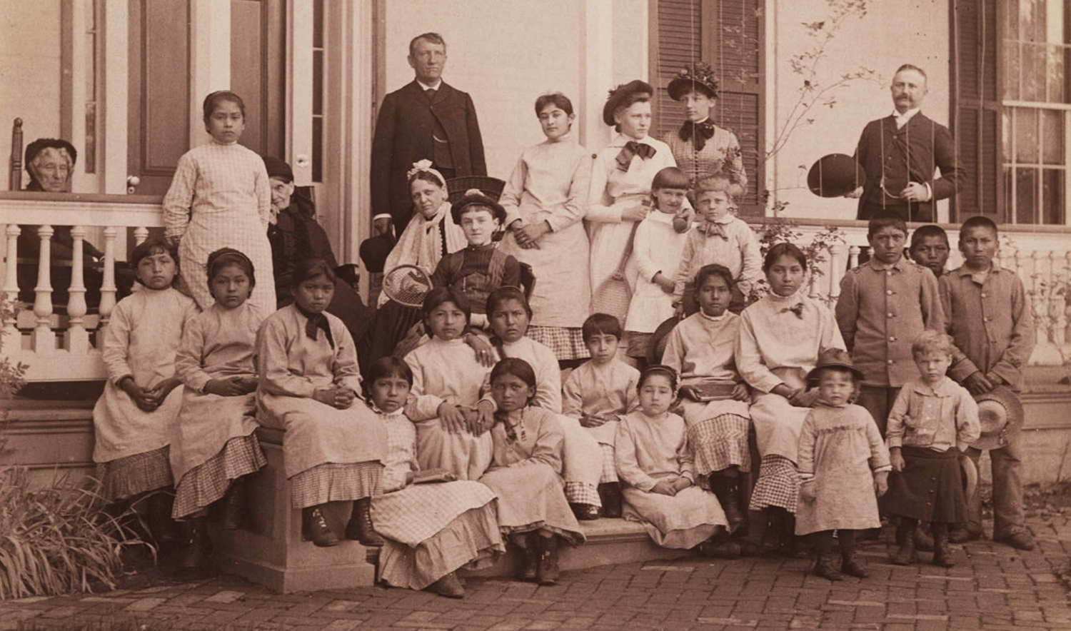Fotografia do Capitão Pratt e alunos da Escola Industrial Carlisle, impressão fotográfica em preto e branco, 13 cm x 21,5 cm. O capitão Richard Henry Pratt serviu como chefe da Escola Industrial Carlisle, para onde os nativos americanos foram enviados. Imagem fotografada por volta de 1900 (sem data). Pratt morreu em 1924. Cortesia da Coleção de Yale de Western Americana, Biblioteca de Livros Raros e Manuscritos de Beinecke, Universidade de Yale, New Haven, Connecticut. Domínio público via Wikimedia Commons.