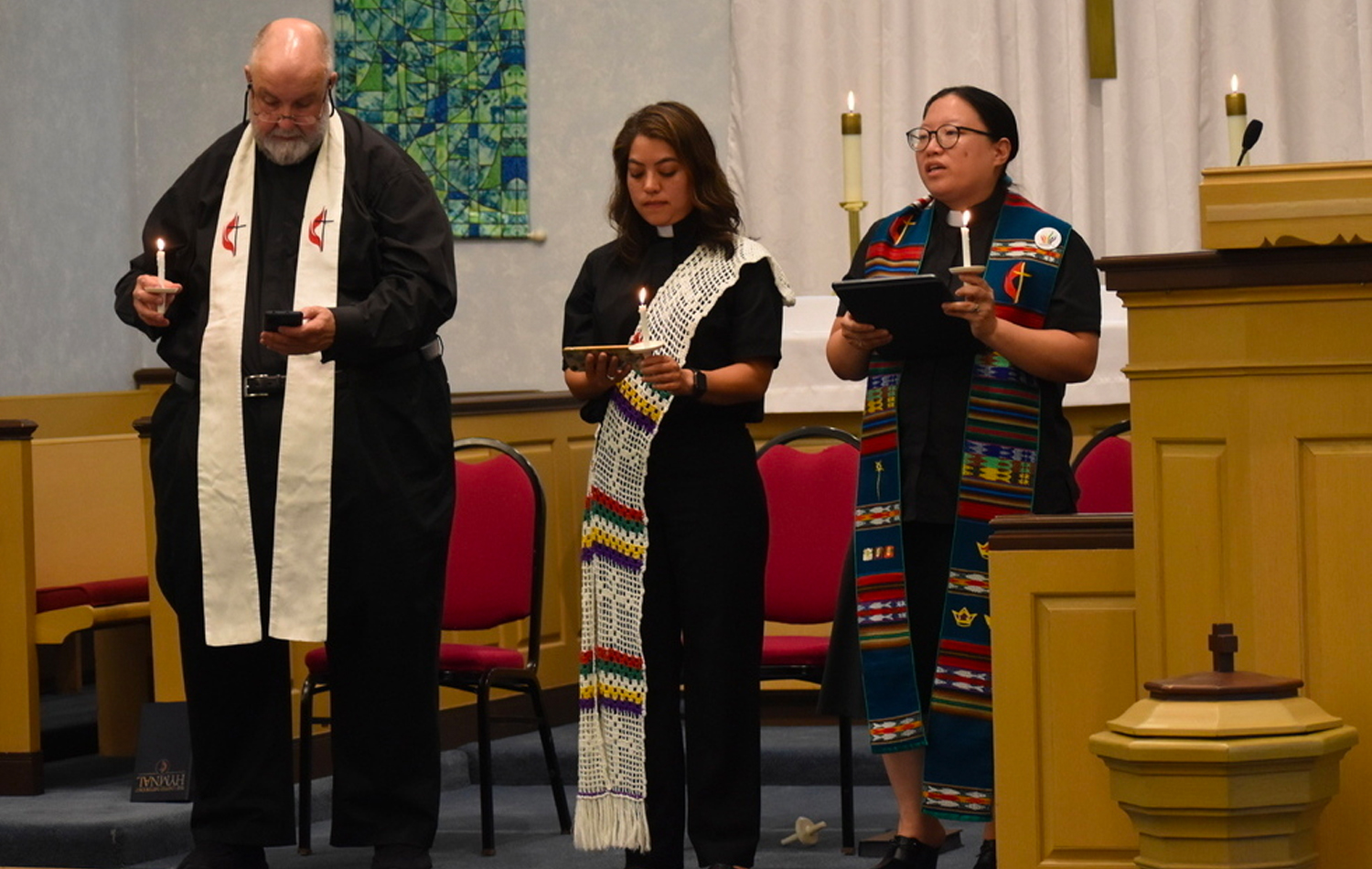 Durante uma vigília de oração em 5 de julho, o Rev. Cal Haines de Lake Bluff, Diácono Patricia Bonilla de Grace UMC e o Rev. Esther Lee, da Christ UMC em Deerfield, segure velas e lembre-se das vítimas e feridos no desfile de 4 de julho em Highland Park. Foto cortesia da Conferência Anual do Norte de Illinois.