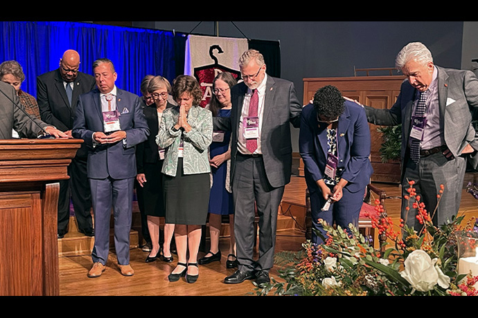 Newly elected United Methodist bishops David Wilson (third from left, wearing blue jacket), Laura Merrill (wearing green print jacket) and Delores “Dee” Williamston (second from right) are joined by other bishops and church leaders as they pray after being elected during the South Central Jurisdictional Conference in Houston. On Nov. 3, the jurisdiction announced its episcopal assignments, effective Jan. 1. Photo courtesy of the Great Plains Conference.