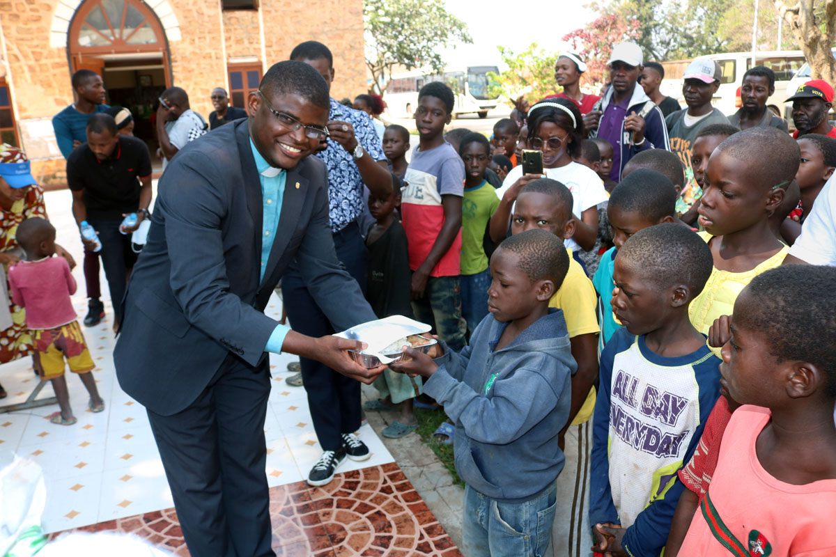 O Rev. Manuel Calimbue simbolicamente entrega a tigela com comida   ao primeiro menino no pátio da Igreja Central de Malanje, Angola. Foto de João Goncalves Nhanga.