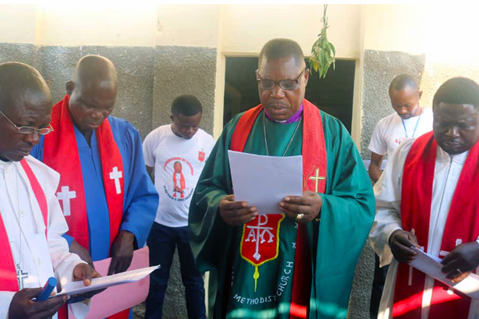 L'évêque Daniel O. Lunge, évêque résident de la région du Congo Central, prononce une prière de dédicace dans une nouvelle Église Méthodiste Unie dans le camp de personnes déplacées de Nkonko à Kananga, au Congo. Il est entouré de dirigeants méthodistes unis du district de Kinshasa et de la conférence annuelle du Kasaï. Le camp abrite des Congolais qui ont été expulsés d'Angola après avoir fui vers ce pays en 2017 dans un contexte d'insécurité. Photo par Cédrick Okandjo, UM News.