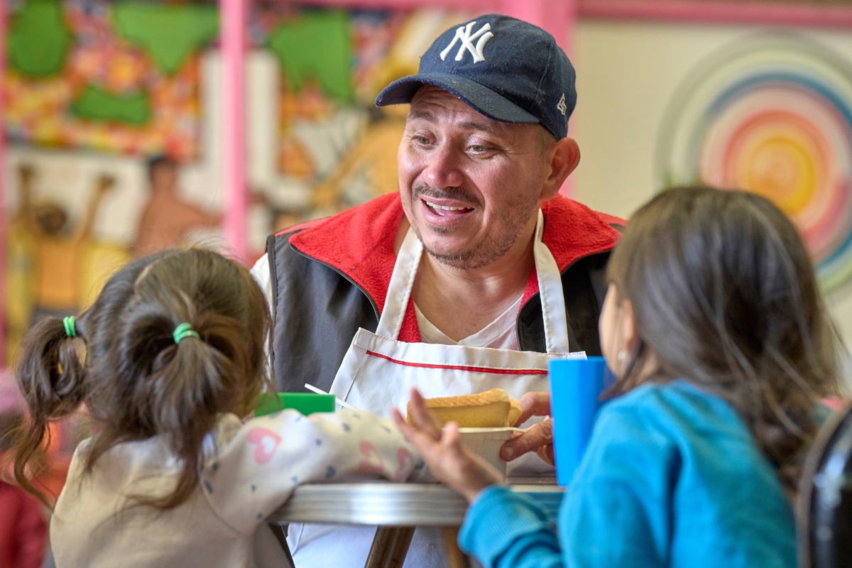 Victor Lugo, a migrant from Venezuela, talks with two of his granddaughters at CAFEMIN, a migrant shelter in Mexico City. Founded by the Josephine Sisters, a Catholic religious order, the shelter has been overwhelmed in recent months by requests for shelter and other forms of assistance. Lugo, who volunteers in the shelter's kitchen, is traveling with seven family members, including the two girls. They are awaiting an appointment with Mexican immigration officials, hoping for a transit visa that will allow them to proceed further north. Photo by the Rev. Paul Jeffrey, UM News.