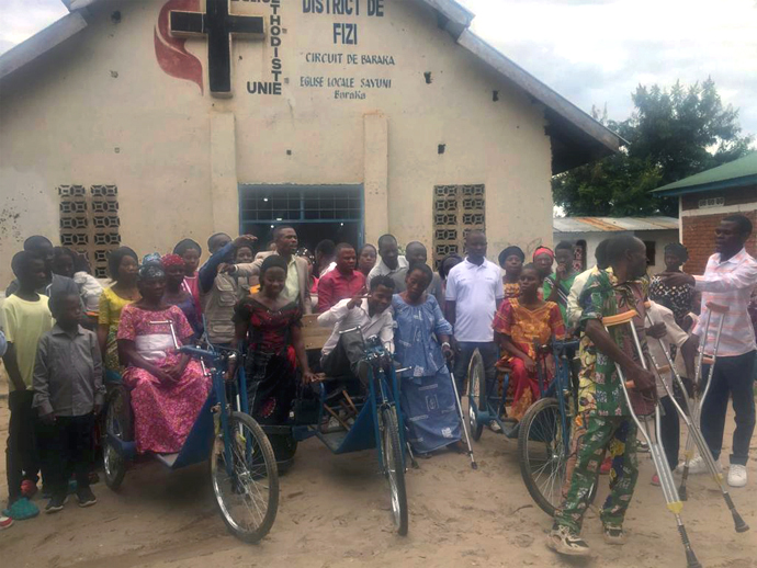 Lusambya Byammese (center), a member of the Salvation Choir at Sayuni United Methodist Church in Baraka, Congo, poses with other recipients of mobility aids from The United Methodist Church in Congo. Byammese said the new tricycle will enable him to get around more easily and continue singing for God. Photo by Philippe Kituka Lolonga, UM News.