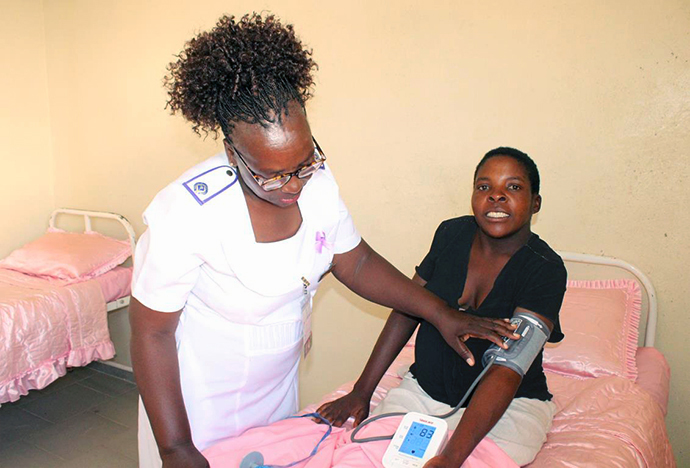 La responsable Mildred Marimbire encourage Kudzai Chimwamwa à se détendre pendant qu'elle prend sa tension artérielle à la clinique de la mission Munyarari de l'Église Méthodiste Unie à Munyarari, au Zimbabwe. La future mère Chimwamwa, qui habite à environ 8 km de là, est hébergée dans le nouveau centre d'accueil des mères en attente de la clinique. Photo par Kudzai Chingwe, UM News.