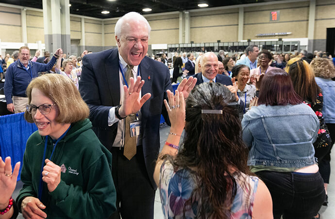 Bishop Thomas J. Bickerton high-fives delegates, visitors and staff of the United Methodist General Conference in Charlotte, N.C., who are dancing in the aisles following morning worship on the final day of the conference. Behind him is Bishop John  Schol. Photo by Mike DuBose, UM News.