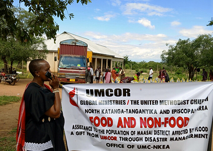 Le pasteur Paulina Koinasai de l'Église Méthodiste Unie de Kambala, dans le district de Masai, tient une affiche annonçant la distribution de nourriture et de produits non alimentaires aux victimes des inondations dans la région. Photo gracieusement fournie par le bureau de gestion des catastrophes de la Région Épiscopale du Nord Katanga.