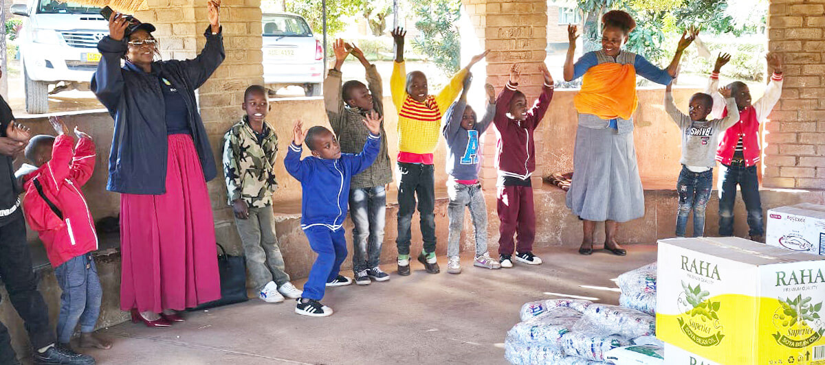 Florence Kachingwe (left, in pink skirt), chairperson of The Class of 81 Charitable Foundation, sings and dances with kids at Fairfield Children’s Home, a United Methodist-affiliated children’s home in Mutare, Zimbabwe. The foundation, started by former students at United Methodist Hartzell High School, donated food and other supplies to the school. Photo by Tafadzwa Gumbochuma.