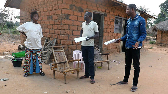 Michel Tahindja Tashinga (centro) e Kitete Kahodi, estafetas de saúde da comunidade Metodista Unida, falam sobre varíola com um residente da aldeia de Dikungu em Kibombo, Congo. A dupla tem andado de porta em porta nas suas comunidades para aumentar a consciencialização sobre a varíola e para encorajar a procura de cuidados médicos adequados. Foto de Chadrack Tambwe Londe, Notícias da MU.