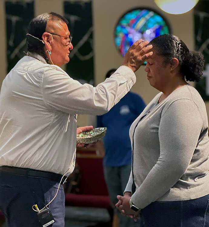 The Rev. Calvin Hill, a Navajo holy man and pastor at First United Methodist Church in Newcastle, Wyo., puts cedar ashes on Dana Lyles, lead of Multiethnic Ministries for the United Methodist Board of Global Ministries, during closing worship Sept. 11 at the 10th Historical Convocation at Bozeman United Methodist Church in Bozeman, Mont. Global Ministries, United Women in Faith and the United Methodist Commission on Archives and History collaborated on a multiyear, multiphase initiative related to boarding schools for Native American children. Photo by Tara Barnes, United Women in Faith.