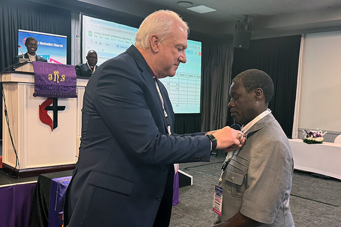O bispo Thomas Bickerton prende a insígnia episcopal metodista unida no colarinho do Rev. Gift Machinga. A Conferência Geral do ano passado elegeu Machinga como membro do Comitê Permanente de Assuntos da Conferência Central. Foto de Priscilla Muzerengwa, Comunicações Metodista Unida.