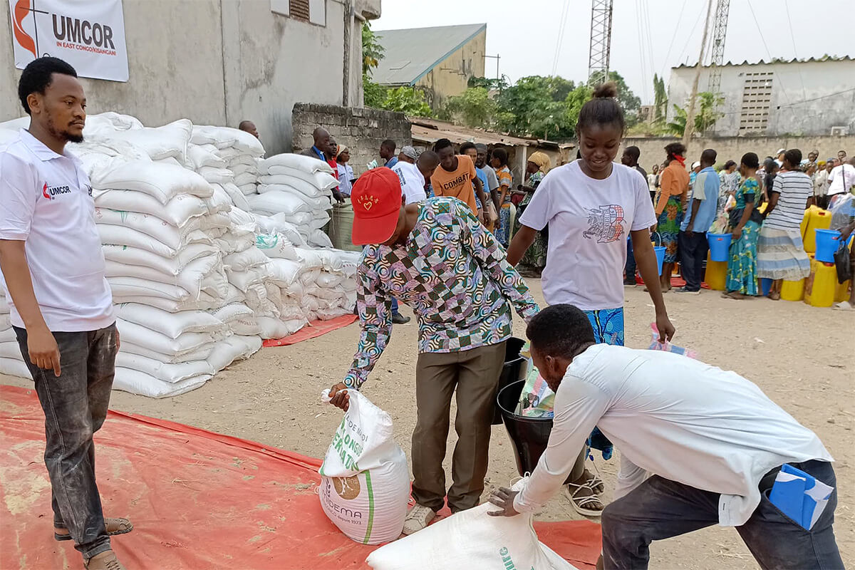 Des bénéficiaires prennent des sacs de riz et de farine de maïs, tandis qu'un volontaire se tient debout lors d'une opération de distribution de nourriture à Kisangani. Grâce à un financement de 150 000 dollars de UMCOR (United Methodist Committee on Relief), l'Église Méthodiste Unie a aidé plus de 10 000 personnes déplacées, soit 1 600 ménages, dans la région de Kisangani. Photo par Lebon Okito, UM News.