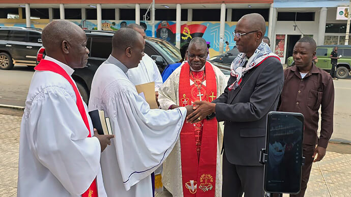 O vice-governador Franco Mufinda (usando terno preto), Saúde oficiais da Conferência à sua Chegada, da direita para esquerda Bispo Moisés Bernardo Jungo com a Stola episcopal, a esquerda saudando Mufinda, Rwv. Rogerio Bartolomeu, Assistente do Bispo, e de seguibda Rev. Pedro Gouveia, Superitendente do Distrito de Malange. Foto de Orlando da Cruz, Notícias da MU. 