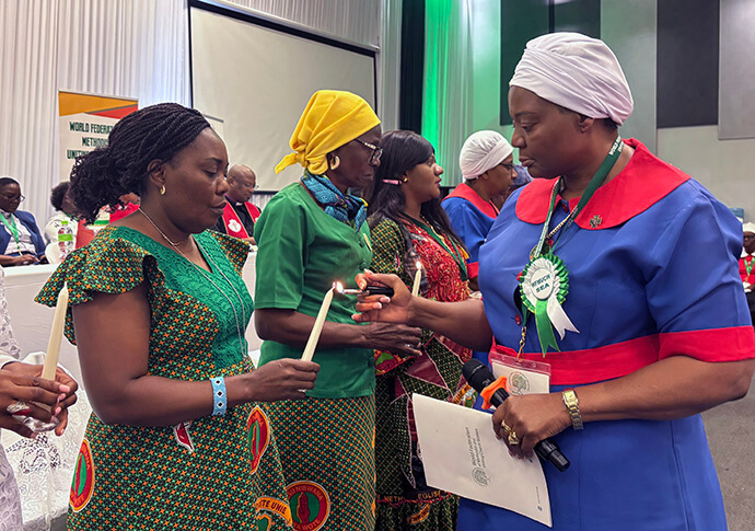 Patricia Mapani (right), a United Methodist and World Federation of Methodist and Uniting Church Women president for Southern and East Africa, lights a candle held by Francine Ilunga Mpanga Mufuk, a Global Ministries missionary, during a service to remember members who passed away since 2023. Photo by Eveline Chikwanah, UM News.