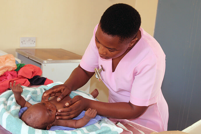 Kudzai Gumbomunda examine Takudzwa Chihwai, âgé de 6 semaines, à la clinique de Chindenga à Mutoko, au Zimbabwe. Le centre de santé rénové dispose désormais de l'électricité, de l'eau, d'un service de consultations externes, d'un abri d'attente pour les mères et de chambres spacieuses. Photo par Kudzai Chingwe, UM News.