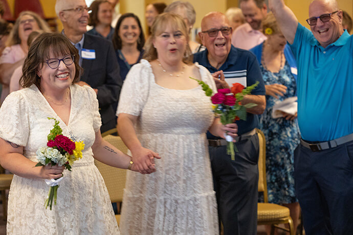 Members of the congregation and invited guests cheer Lindsey Dye (left) and Laura Smotherman after the couple renewed their wedding vows during a Pride Month celebration at Edgehill United Methodist Church in Nashville, Tenn. At right are the Rev. Deen Thompson (in striped shirt) and his husband, John Brown, another of the three couples honored during the event. Photo by Mike DuBose, UM News.