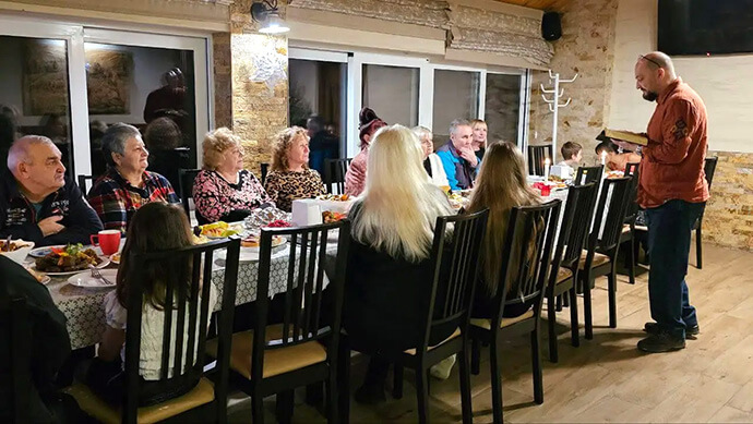 Des Ukrainiens déplacés logés à Under the Castle près de Kam'yanytsya, en Ukraine, prennent un repas ensemble pendant le Noël 2024. Environ 40 personnes sont hébergées dans le centre missionnaire méthodiste uni, qui a été acheté grâce à une subvention du Comité Méthodiste Uni de secours. Photo par la Révérende Yulia Starodubets, avec l'aimable autorisation de Global Ministries.
