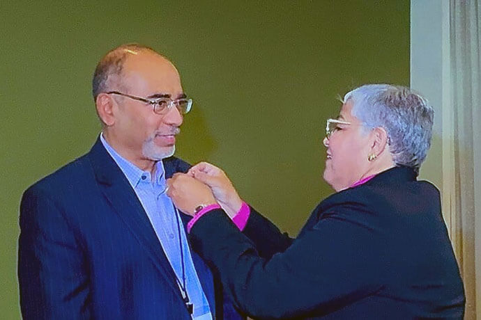 Bishop Lizzette Gabriel Montalvo, episcopal leader of the Methodist Church of Puerto Rico, presents a commemorative button celebrating 125 years of Methodist mission in Puerto Rico to Roland Fernandes, top executive of the United Methodist boards of Global Ministries and Higher Education and Ministry. 