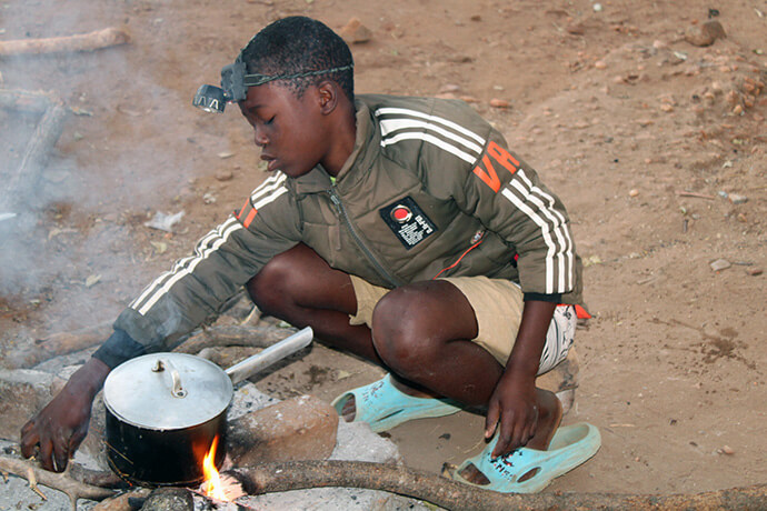 Tanaka Nyarugwe tends to a fire ahead of breakfast at United Methodist Dindi Mission in Zimbabwe. A low-cost boarding school at the mission allows some students to stay on campus rather than walking long distances each day. Photo by Kudzai Chingwe, UM News.